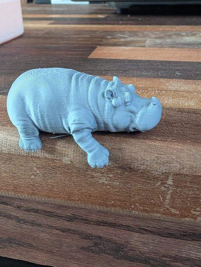 Gray hippo figurine on a wooden surface with a microwave in the background